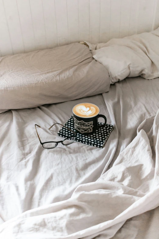 a cup of coffee and some eye glasses on a bed