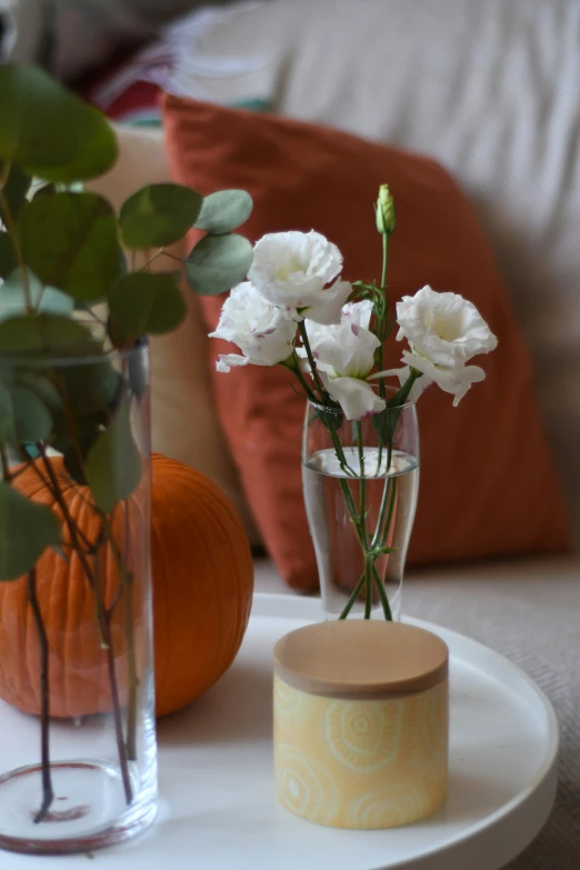 two vases holding white flowers with orange pumpkin behind them
