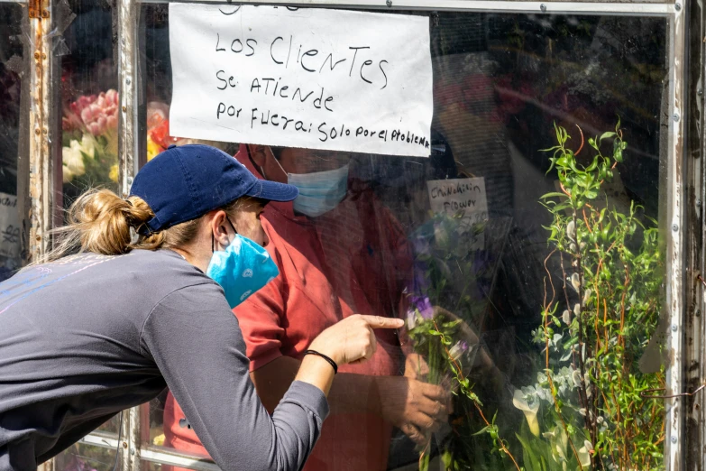 two women standing next to each other wearing masks and pointing at plants