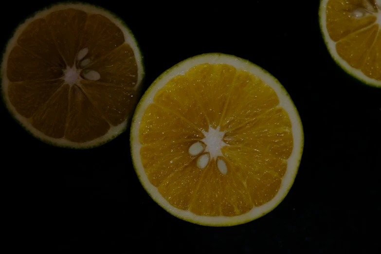 three whole oranges on a black surface
