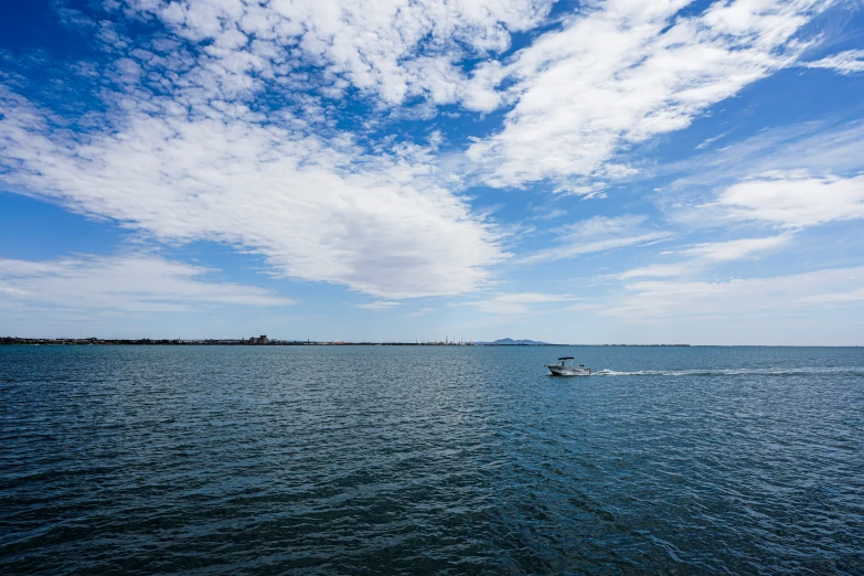 a small boat out on the water under a sky with some clouds