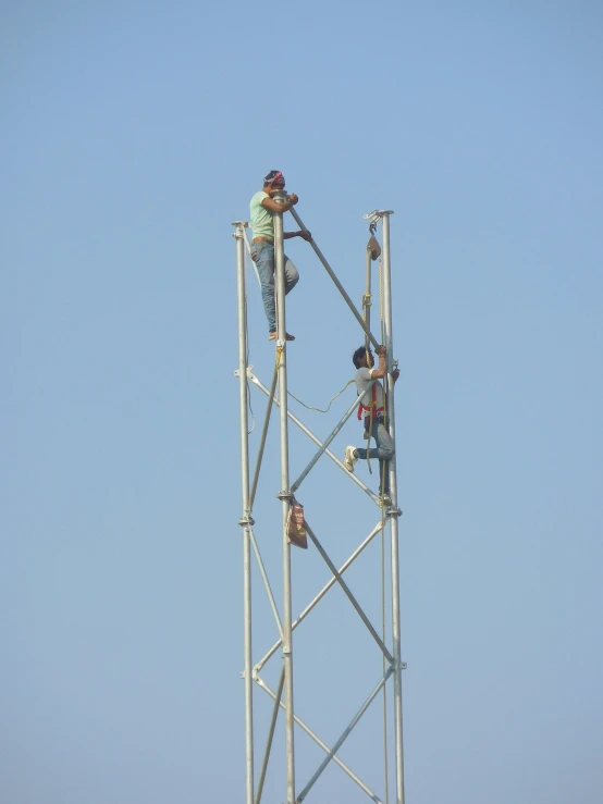 men climbing up the side of a cellular phone tower