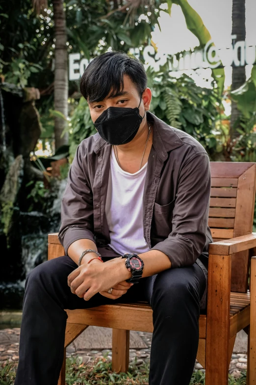 a man sitting on a park bench wearing a black mask