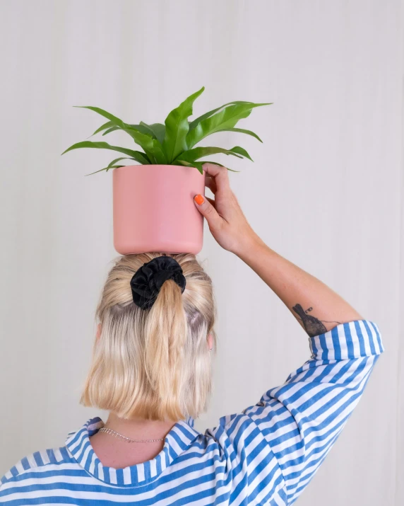 a woman holds up a pot with plant on it