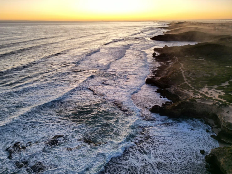 the beach is near many rocky cliffs and the sun sets