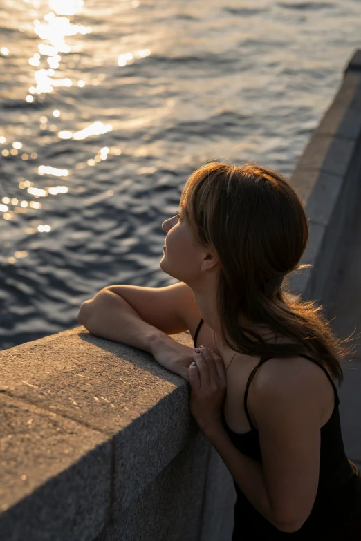 the woman is sitting by the water and looking at the water