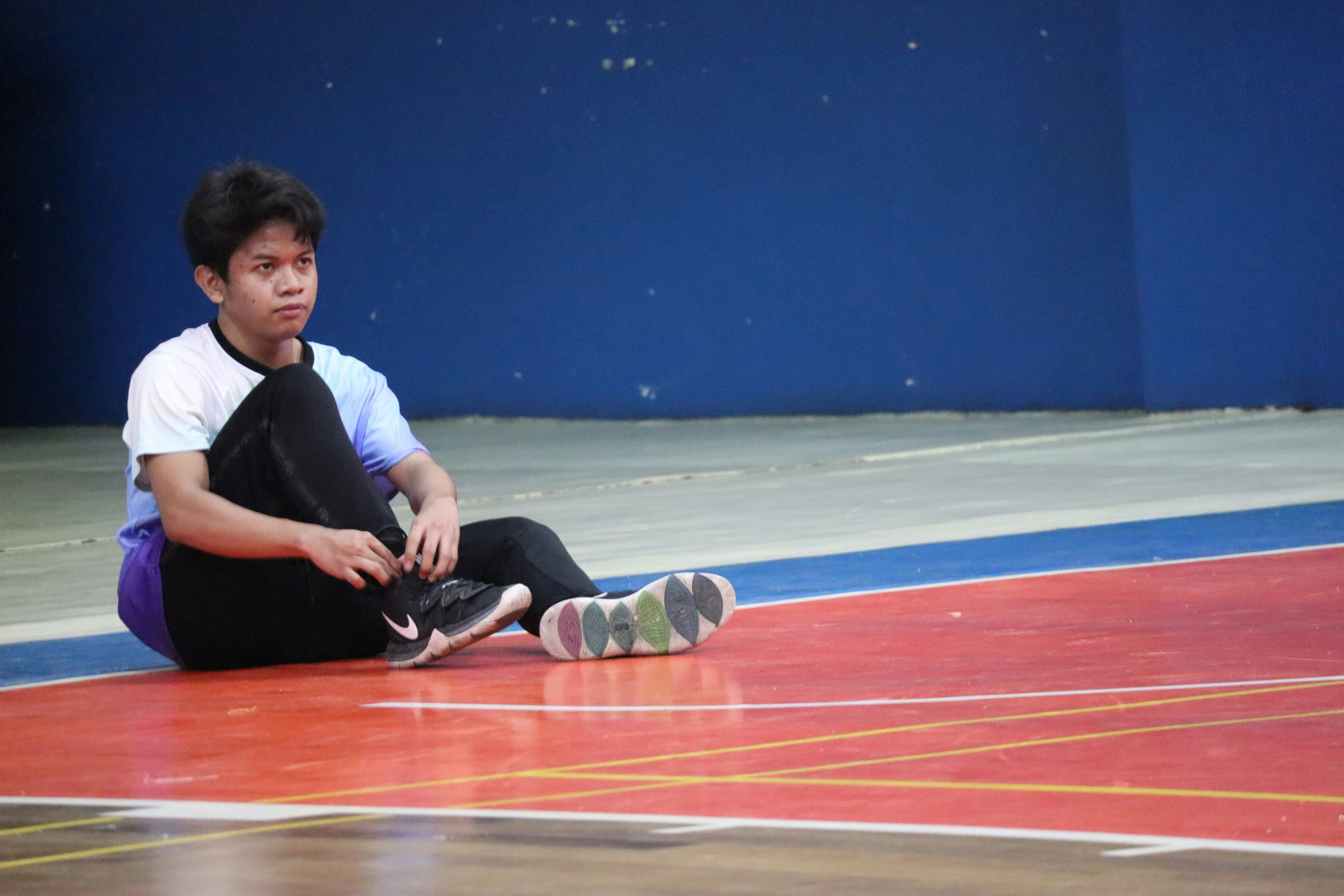 a boy in grey shirt and black pants sitting on basketball court