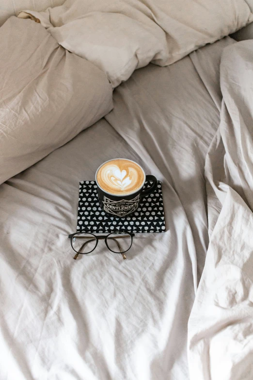 there is a cup of coffee and a cellphone on the bed