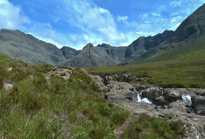 a small stream in a hilly valley with mountains around