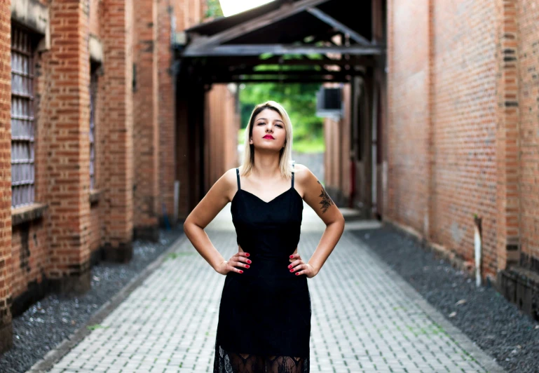 a girl stands in an alleyway in a black dress