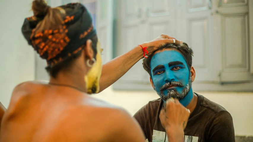 a man with blue paint on his face is shaving another mans face