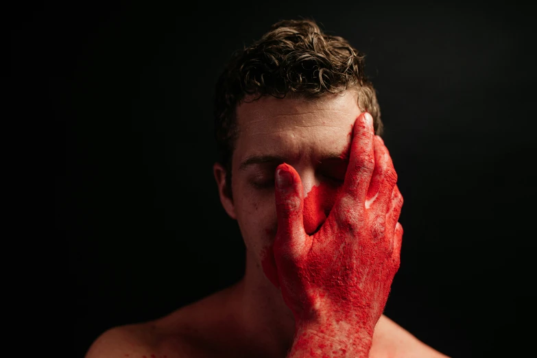 a man with red powder on his face holding his hands up