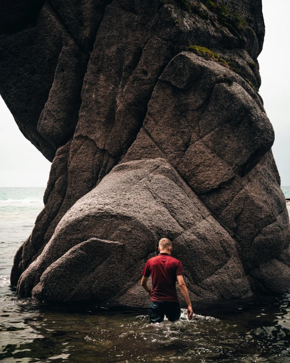 a young man wading through a lake next to large rocks