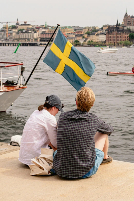 two people sitting on a pier with a flag