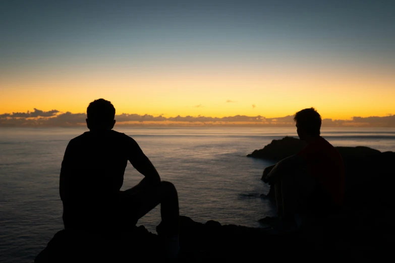 two people sitting in the dark next to the ocean