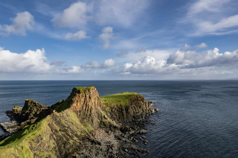 an ocean with clouds above and some green on the shore