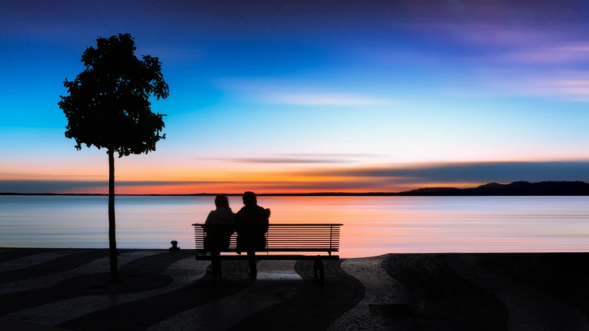 two people sitting on a bench by the ocean
