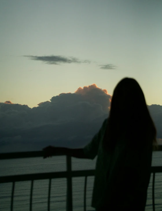 the silhouette of a woman standing on the side of the water