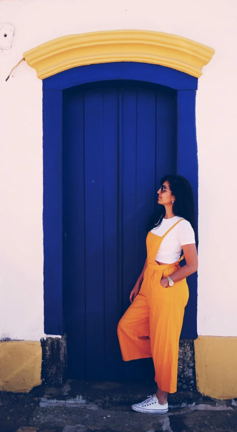 a girl in orange and white is leaning against a blue door