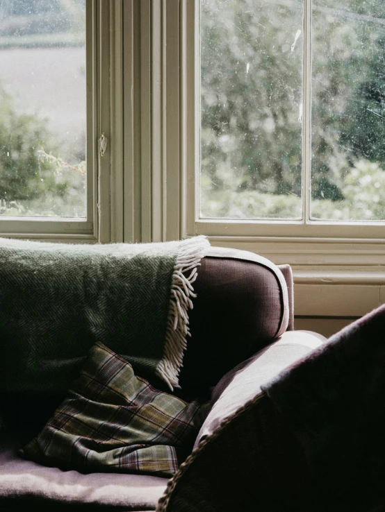 a plaid blanket is sitting on the armrests of a chair near a window