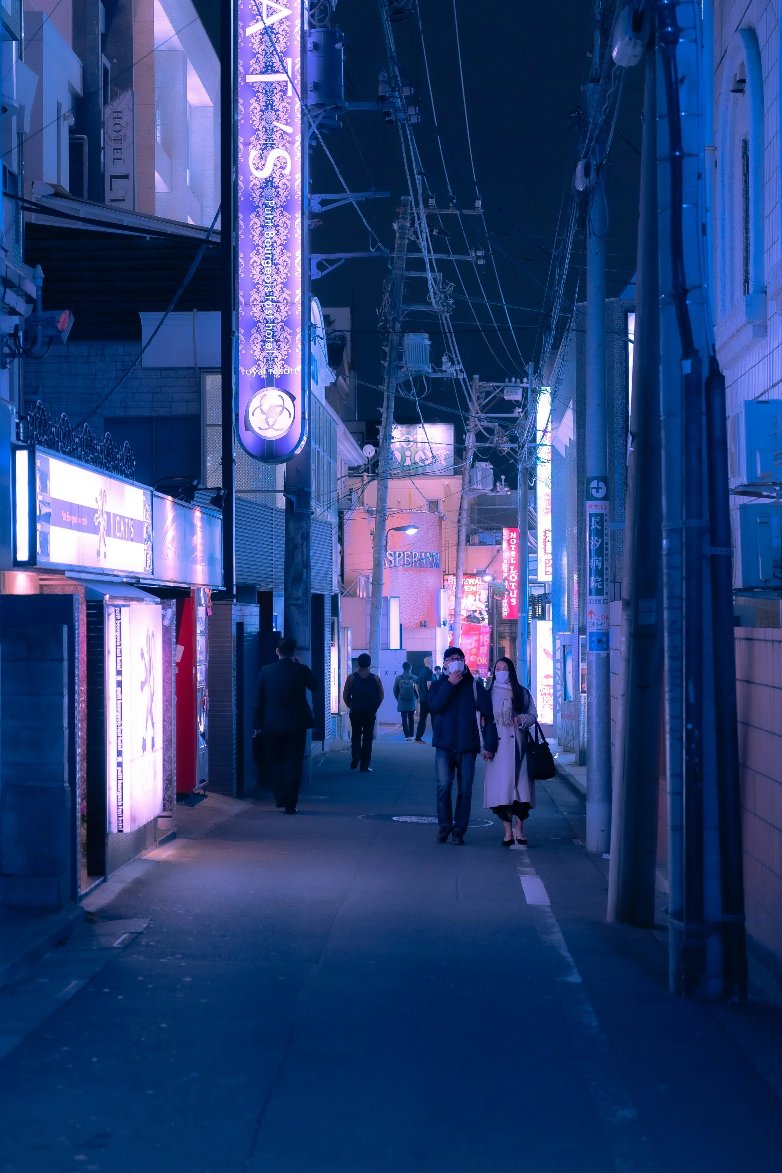 people walking along an alleyway at night with the lights on