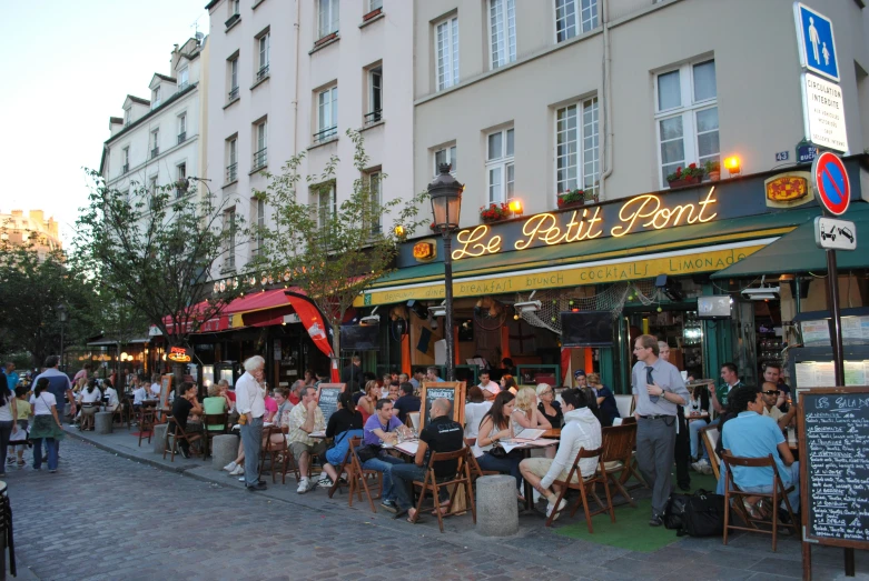 people are sitting at outdoor tables outside an eatery