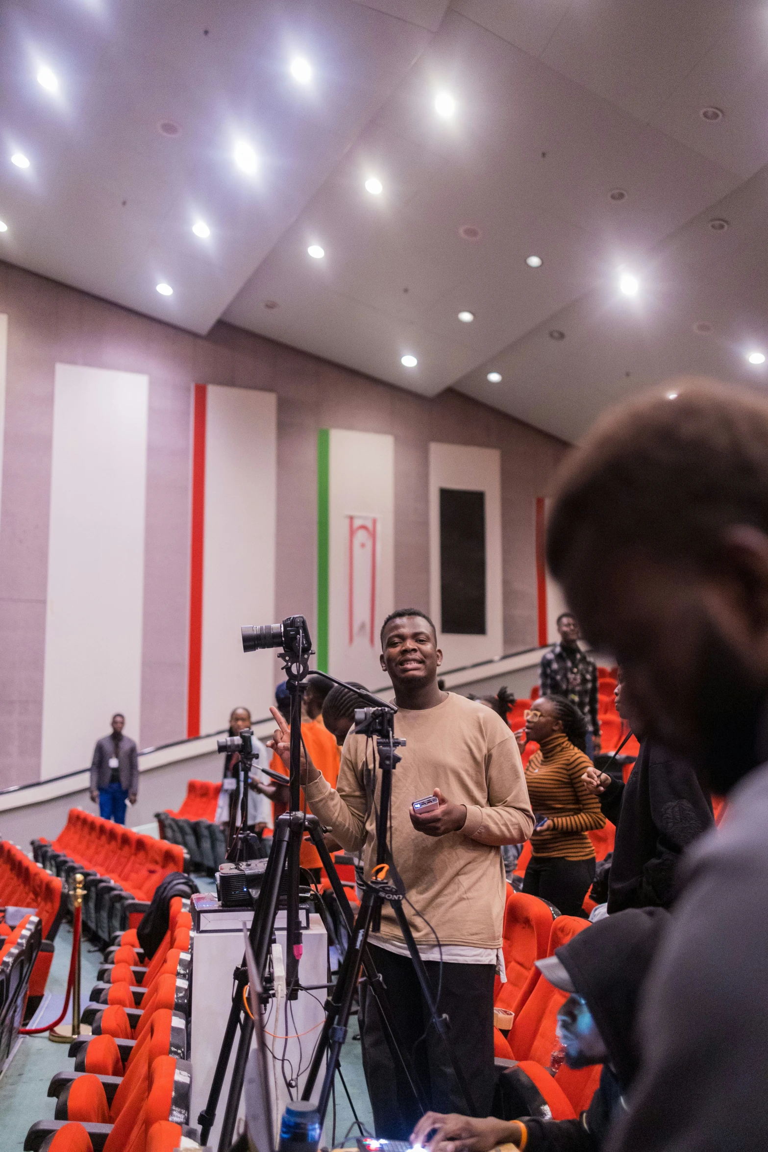 a man stands near a microphone in a room with orange chairs