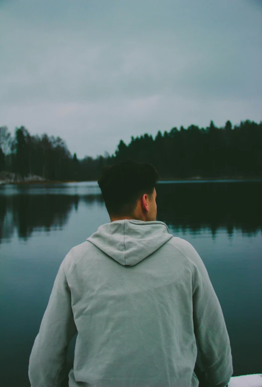 a man in gray hoodie looking at a body of water