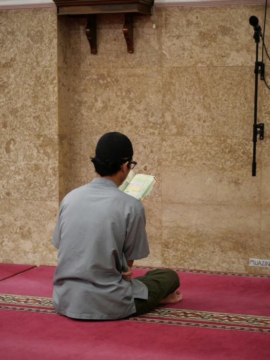 a young man sitting on a rug reading a book