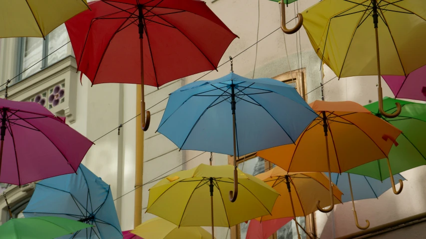 multiple colorful umbrellas attached from wires outside of a building