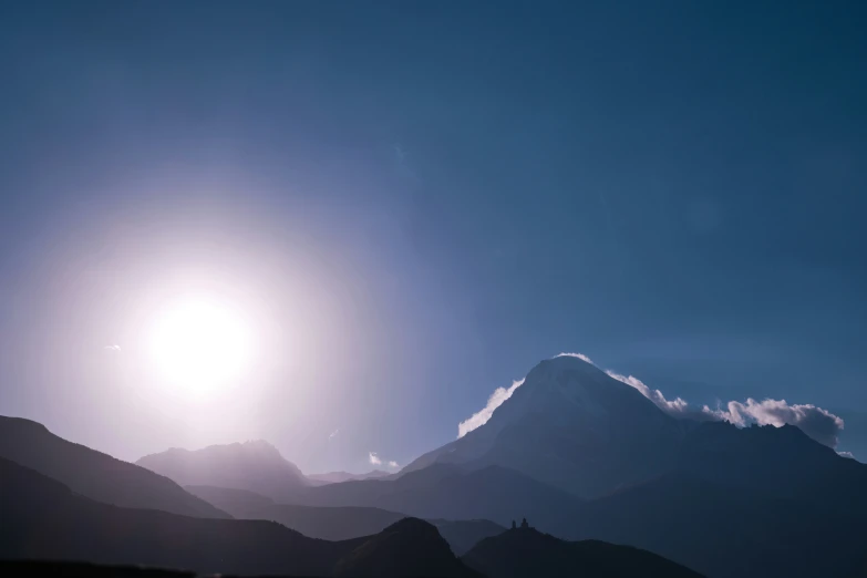 a mountain and a bright sun with some clouds in the background