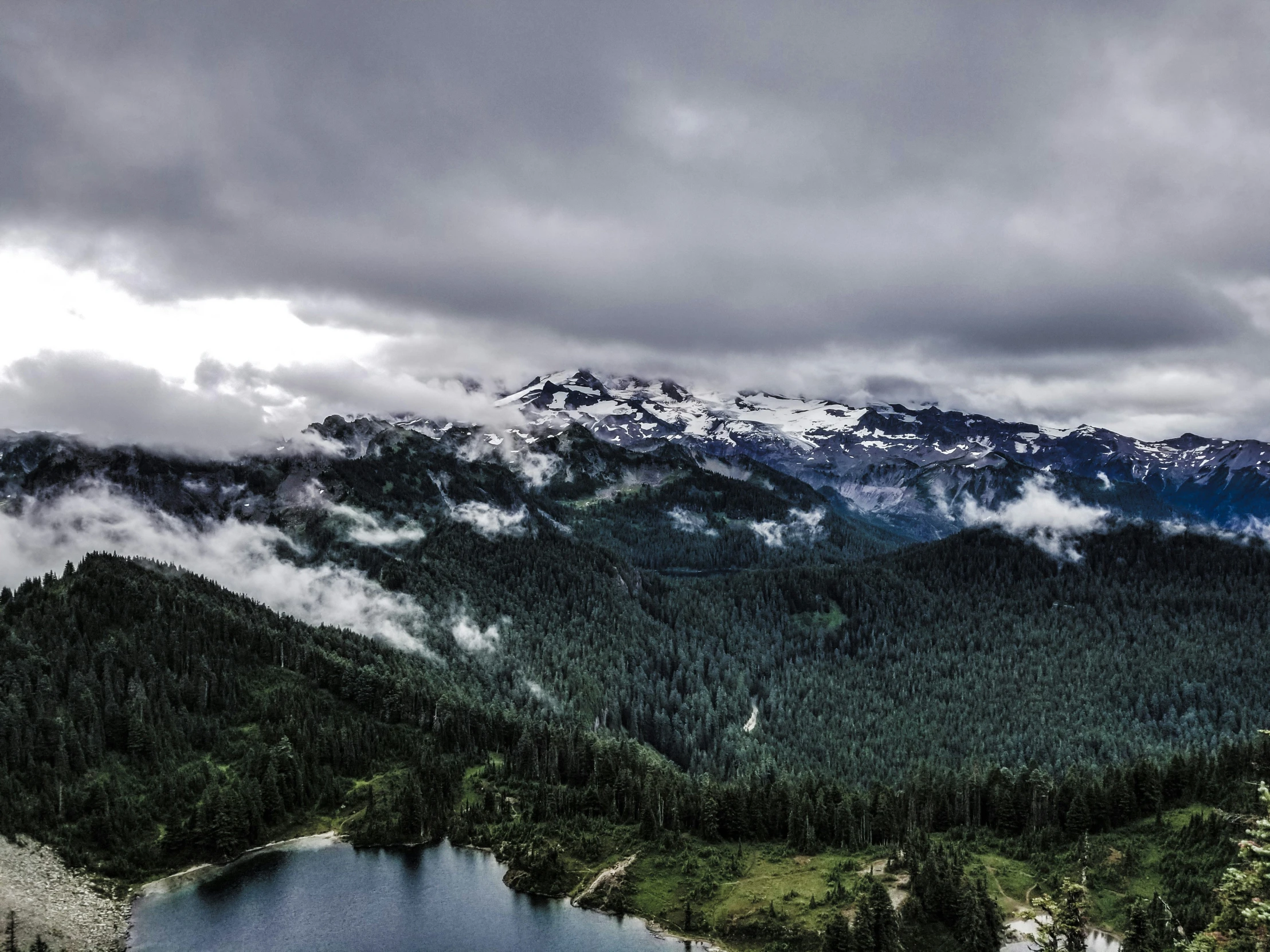 a lake surrounded by green mountains and a cloudy sky