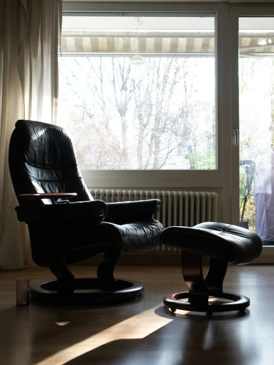 a dark rocking chair with its footrest facing a window