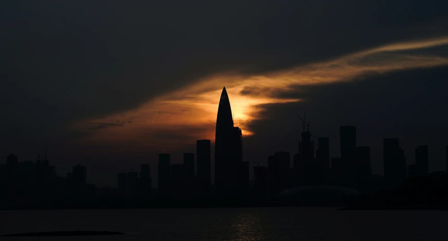 a tall building in a city silhouetted by a setting sun