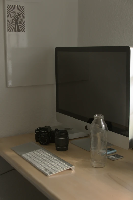 a computer monitor, keyboard, and camera are on the table