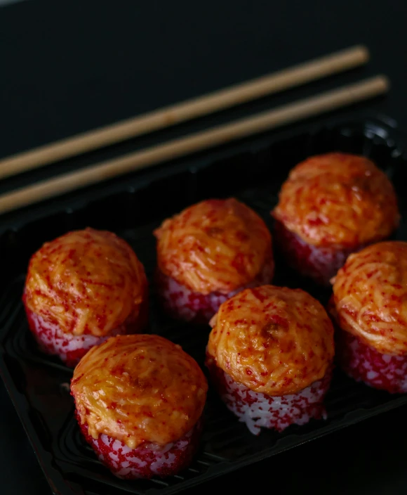 some small round pastry on a black tray next to chopsticks