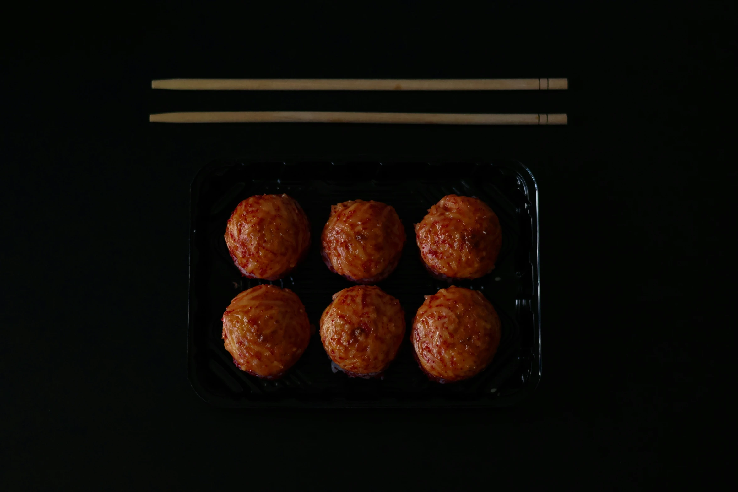 meatballs in a black tray with chopsticks next to it