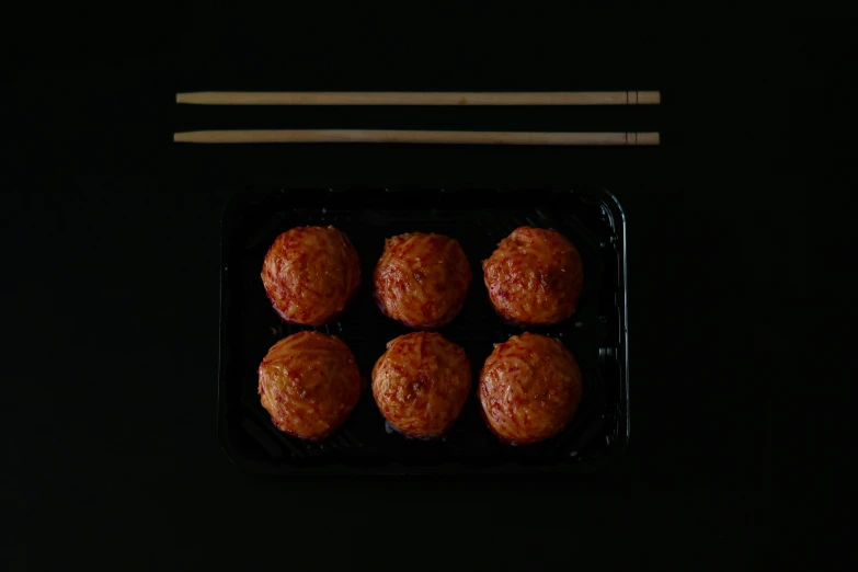 meatballs in a black tray with chopsticks next to it