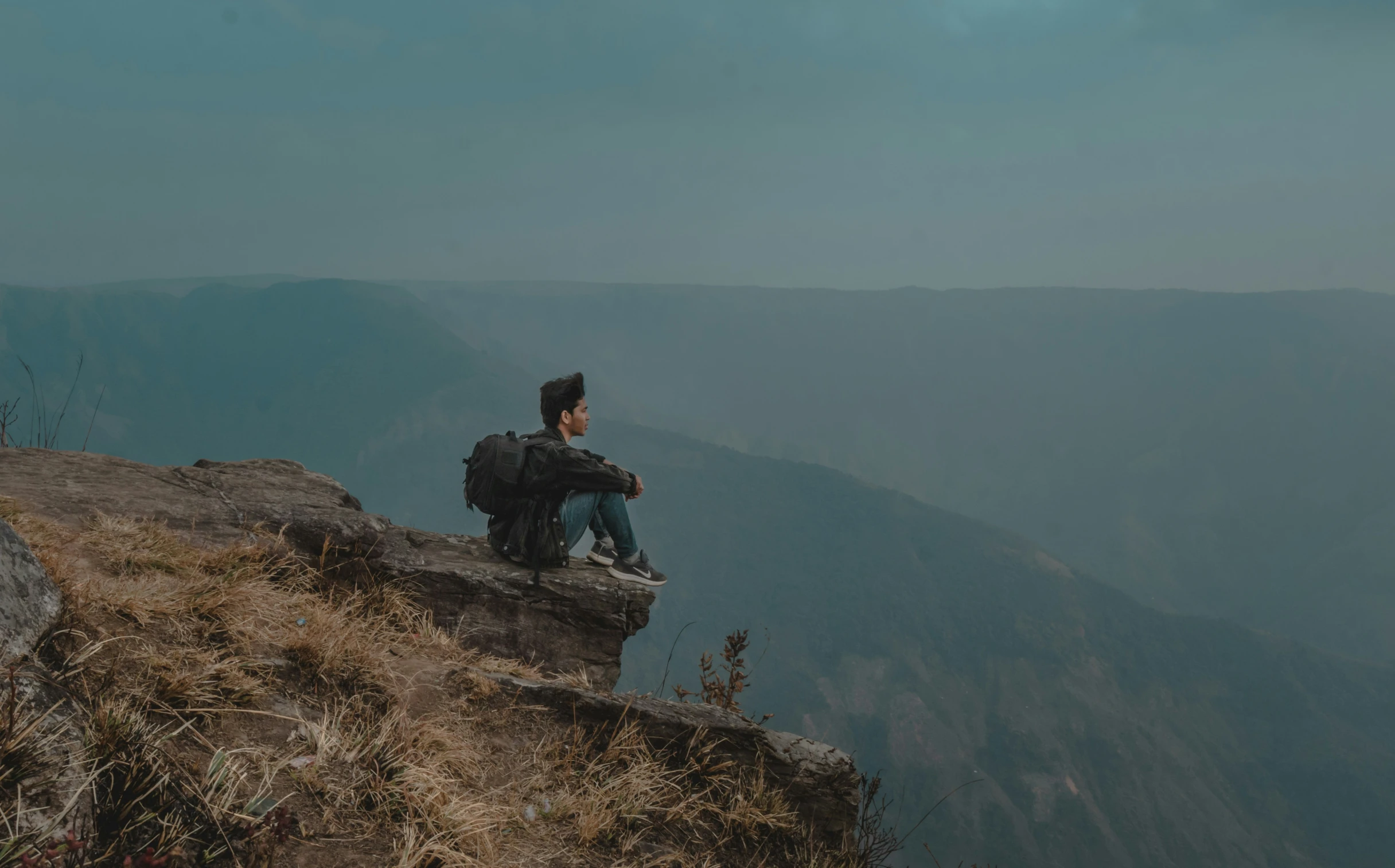 the person is sitting on a rocky hill overlooking the mountains