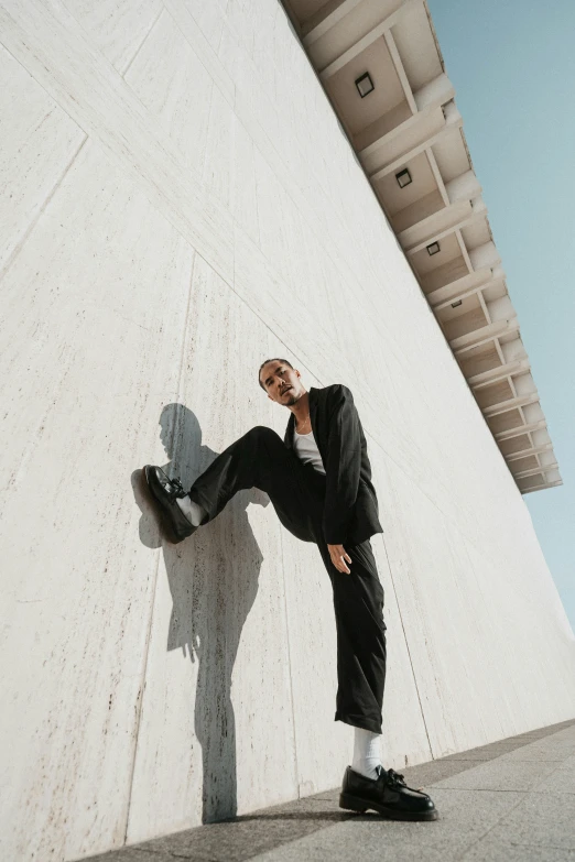 a man in dark clothing leaning against the wall while talking on a cell phone