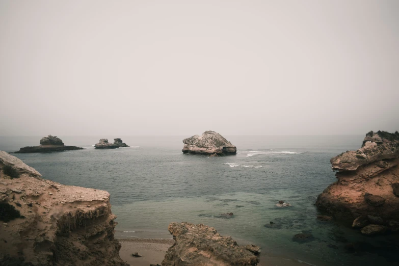 some rocks in the water and fog on a cloudy day