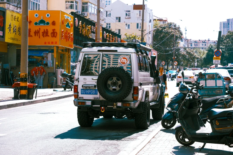 a white jeep and a scooter are in the middle of a busy city street