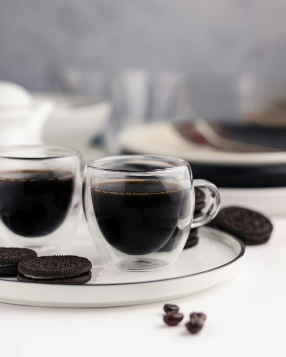 two cups filled with coffee sitting next to chocolate cookies