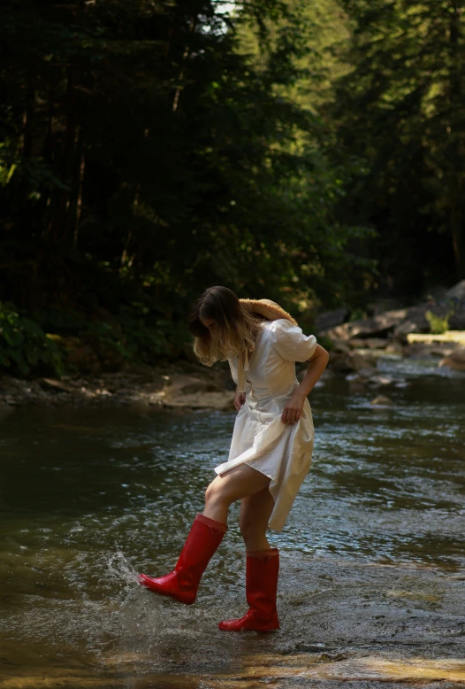 a woman in tall red boots stands near the water