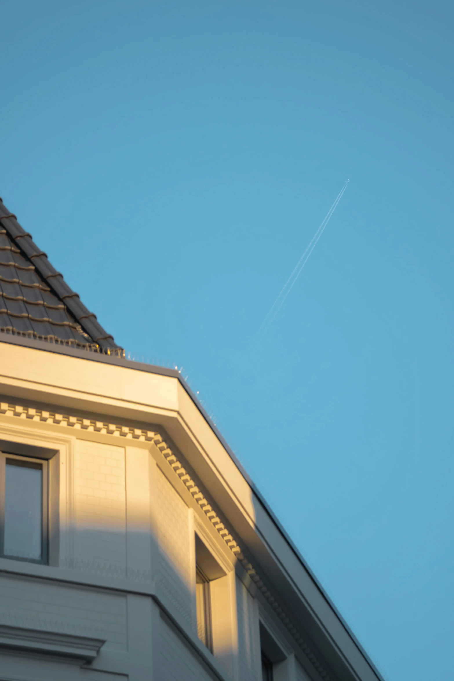 a plane flies overhead by the roof of a building