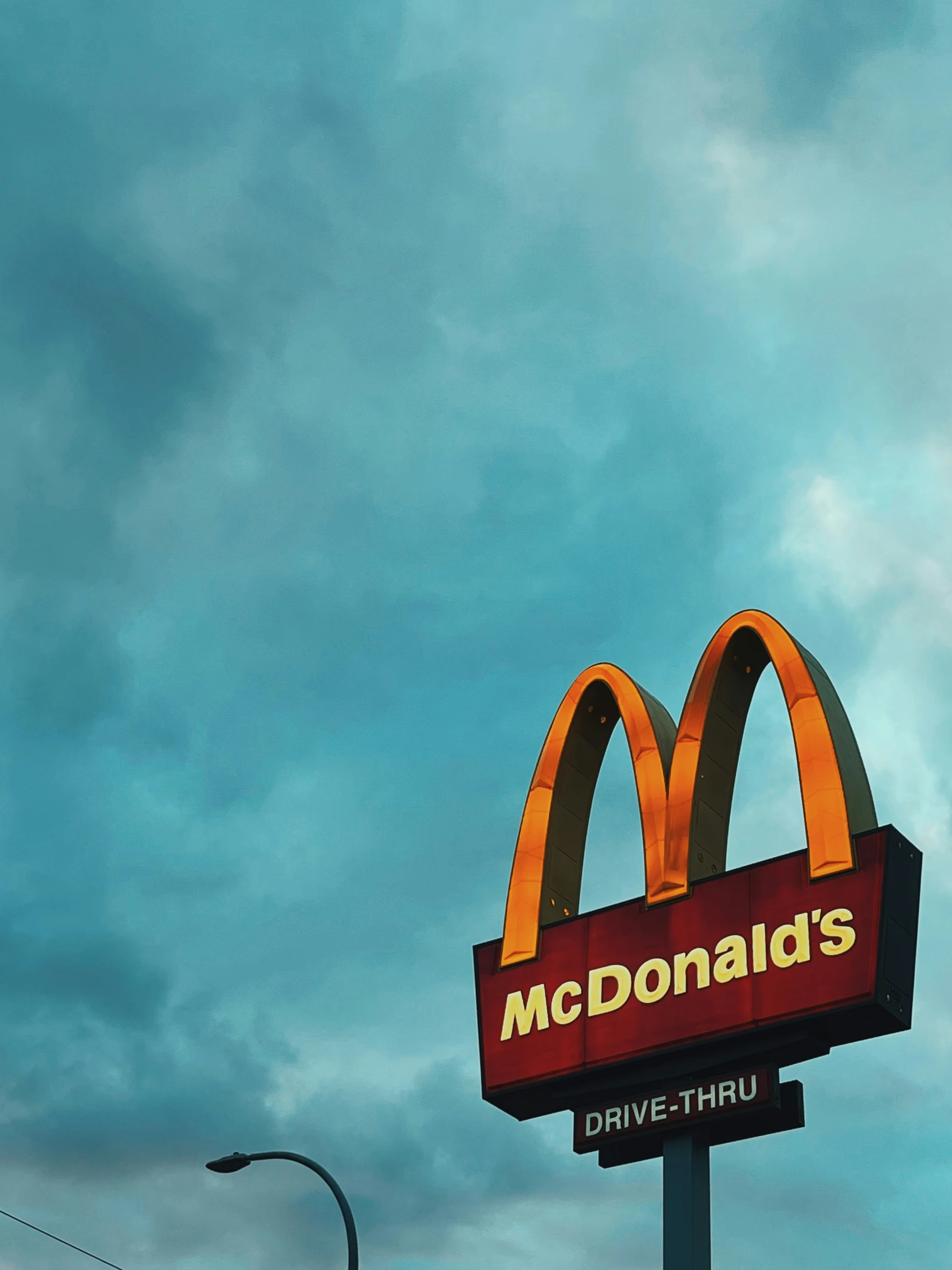 a sign advertising mcdonalds drive thru with a cloudy sky behind it