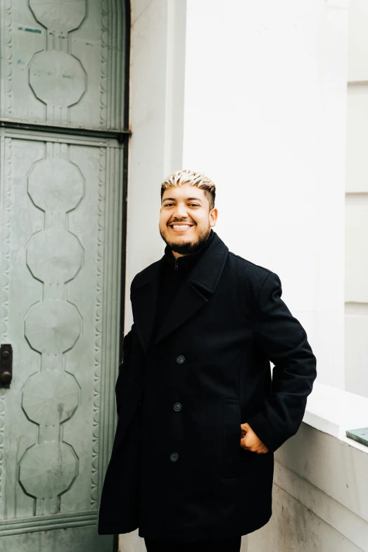 man with hand on hips stands by a gray door