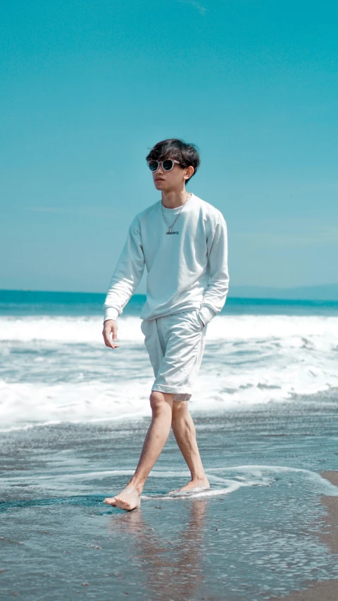 an asian man in white is standing on the sand by the ocean