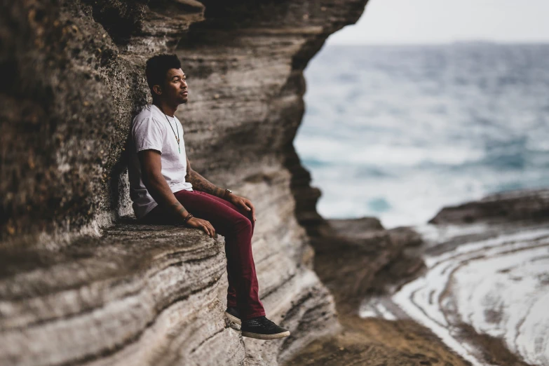 a man sits on a cliff near the ocean
