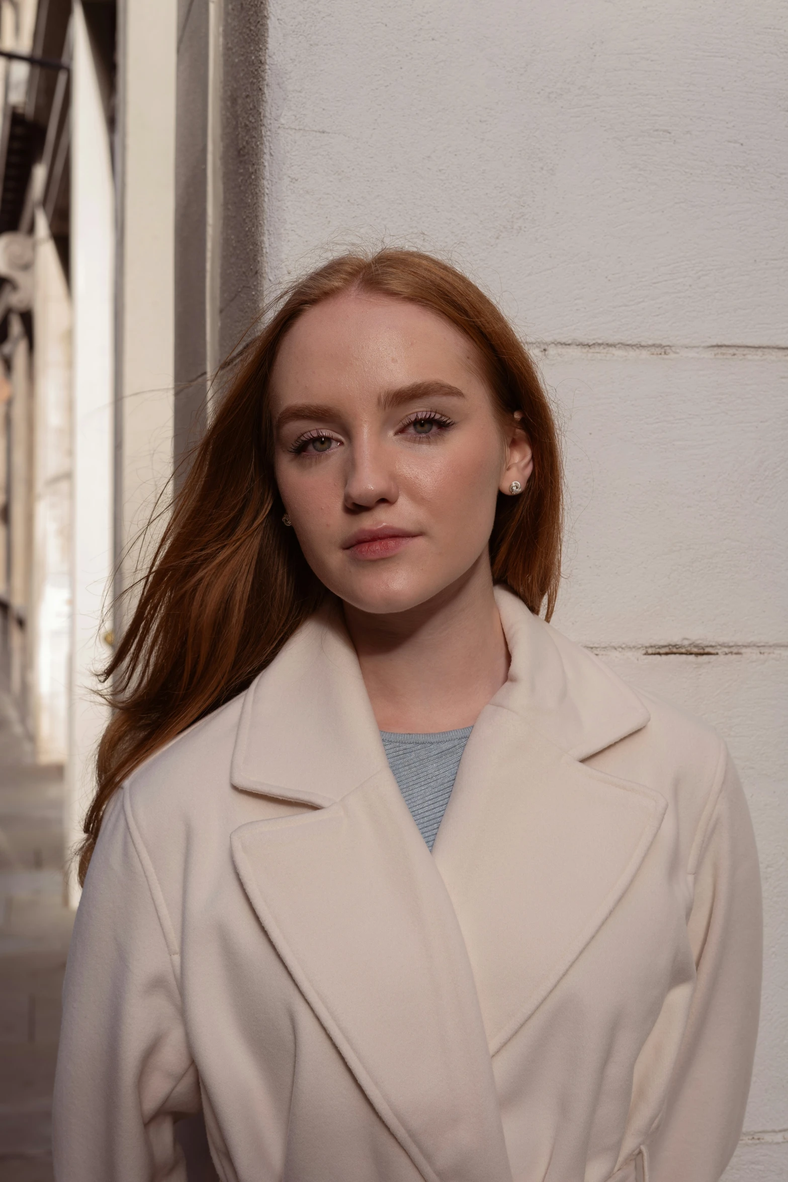 woman with long red hair in trench coat next to wall